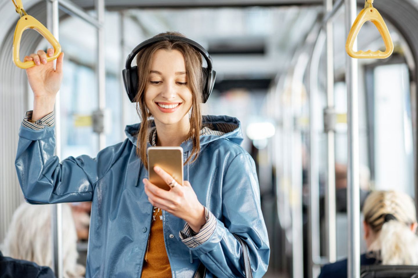 Jonge vrouw staat met koptelefoon en smartphone in een moderne tram