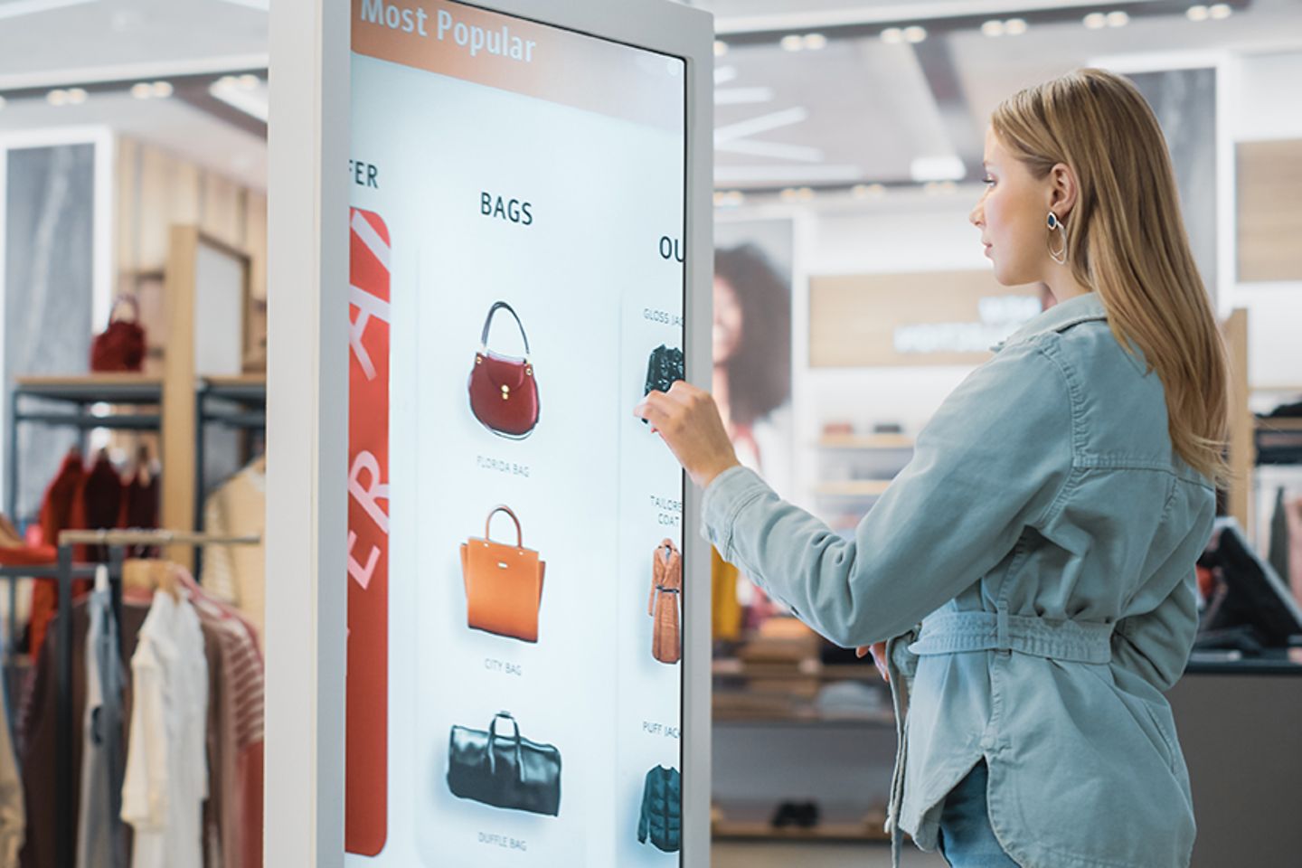 A female customer in a fashion store choosing a bag on a touch screen.