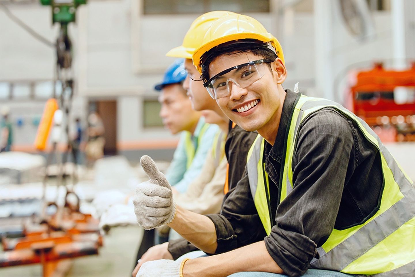 Joven trabajador de fábrica sonriente muestra el pulgar hacia arriba