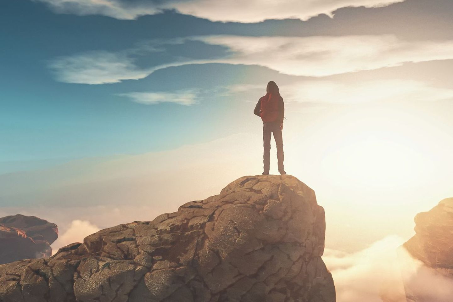 Un homme se tient au sommet d’une montagne entourée de nuages
