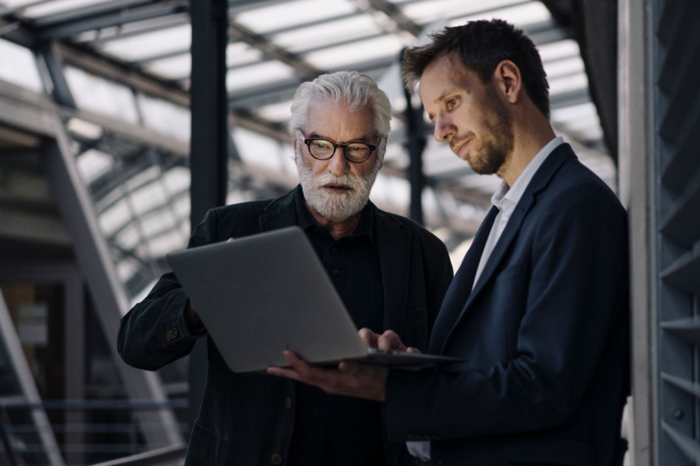 Two businessmen using laptop in office together.