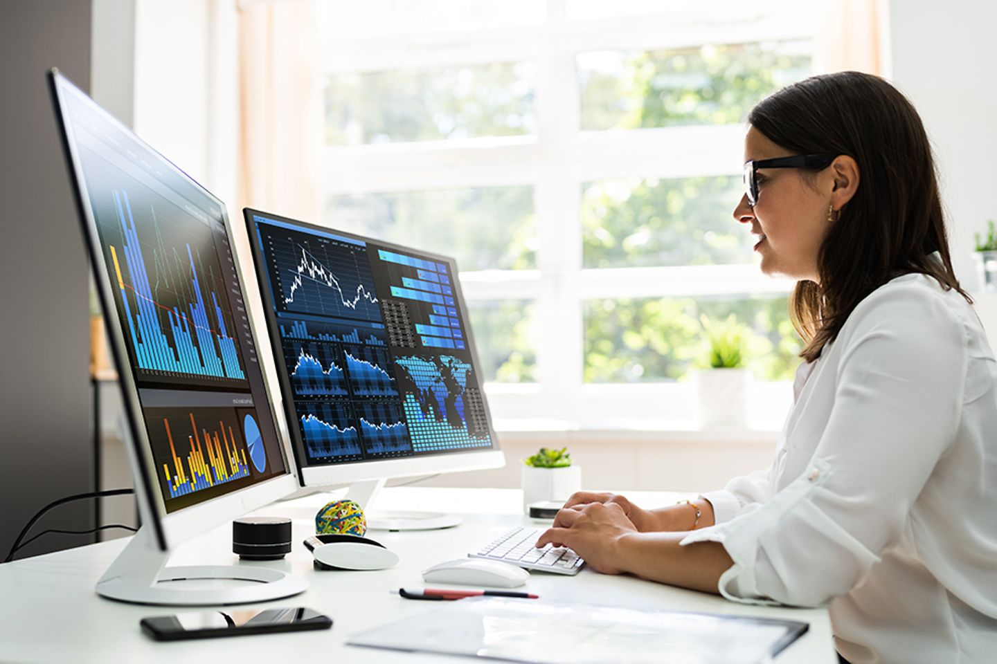 Female professional worker office worker at her desk in the home office with PC screen of data graphs