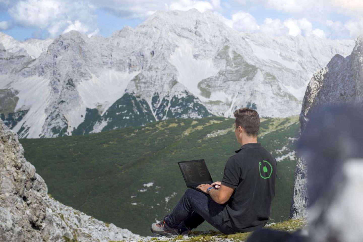 Man sits with laptop in front of mountain scenery