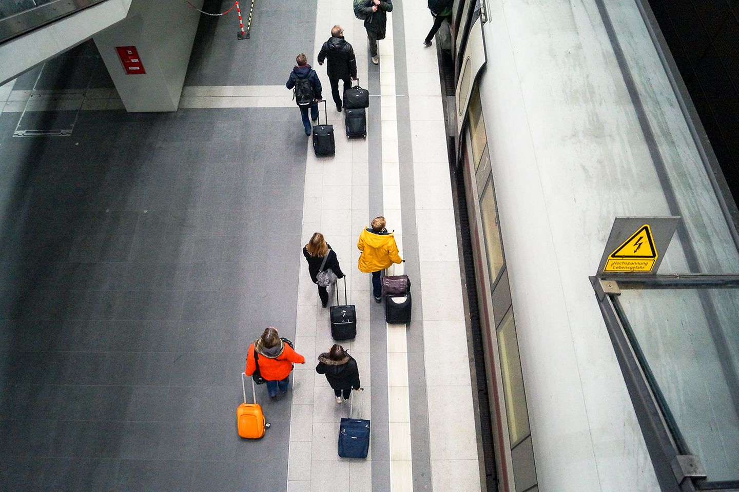 Aerial view of a platform. Travellers pull their bags along next to a waiting train.