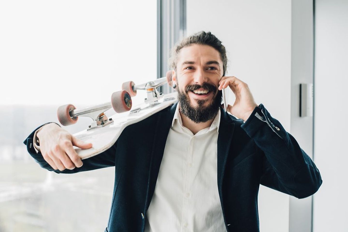 Hipster businessman on mobile phone with skateboard in office
