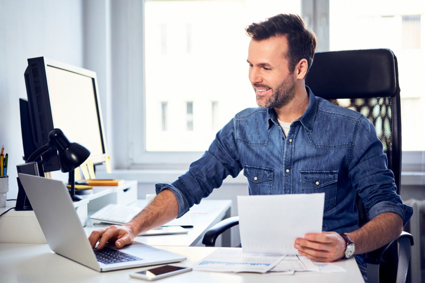  Hombre sonriente sostiene un documento y utiliza un portátil