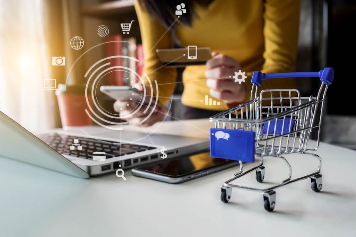 Miniature shopping cart next to laptop and smartphone