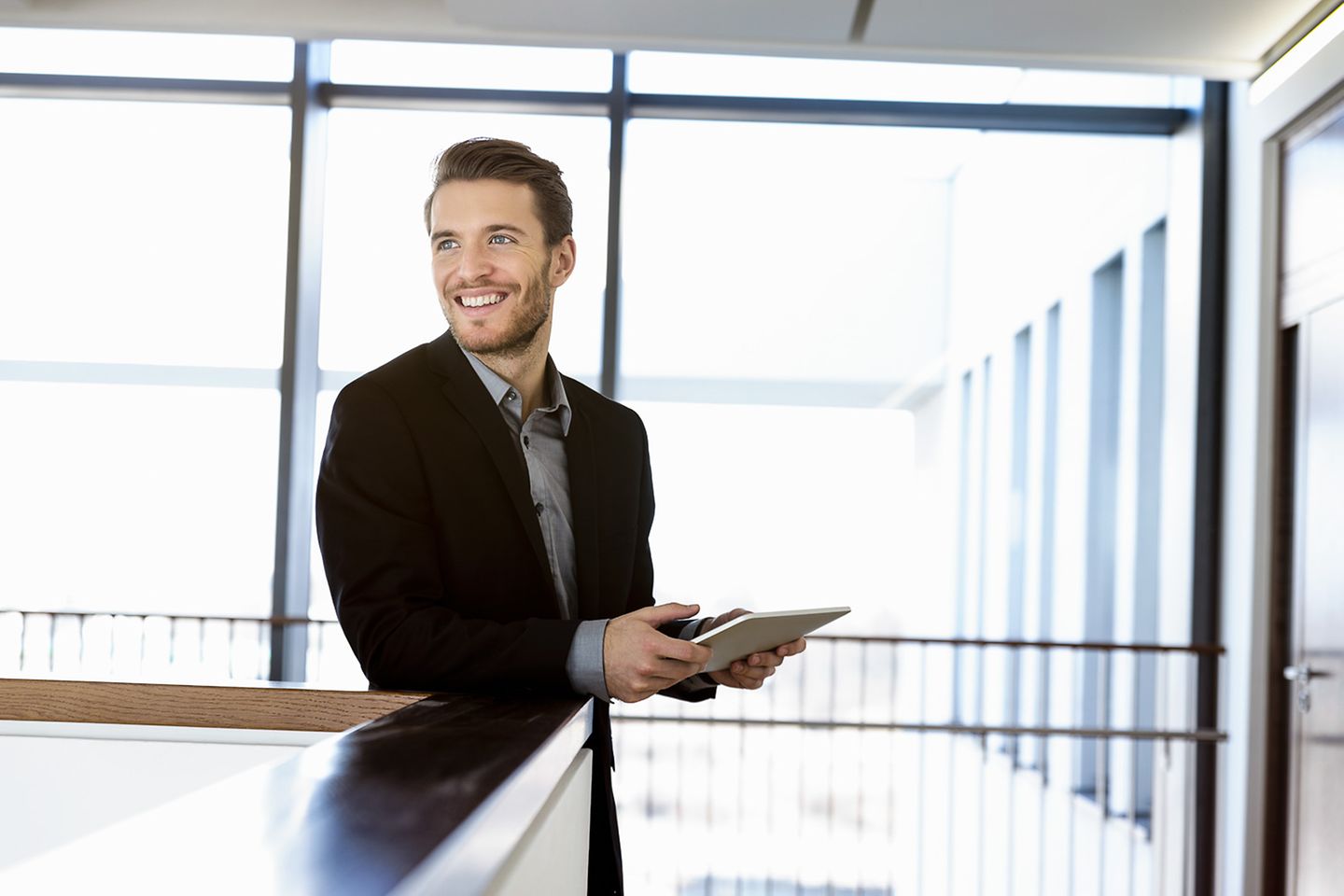 Hombre sonriendo en un complejo de oficinas luminoso con una tablet en la mano