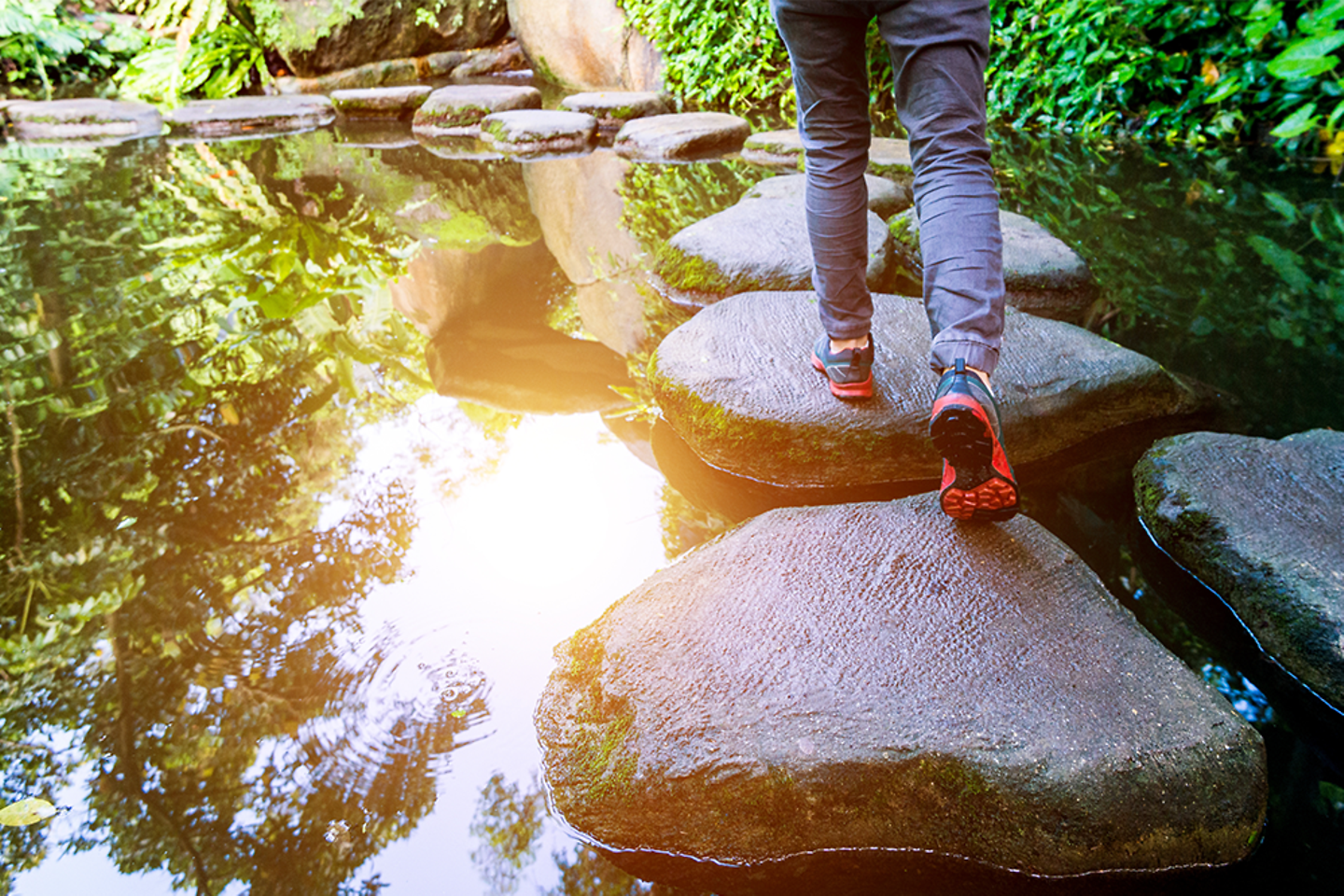 Young man walking crossing a river on stones