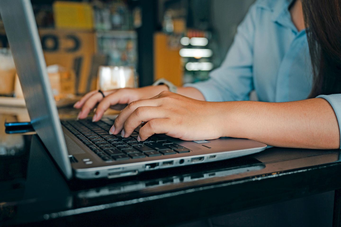 Ein silberfarbenes Notebook, auf dessen Tastatur die Unterarme einer jungen Frau zu sehen sind