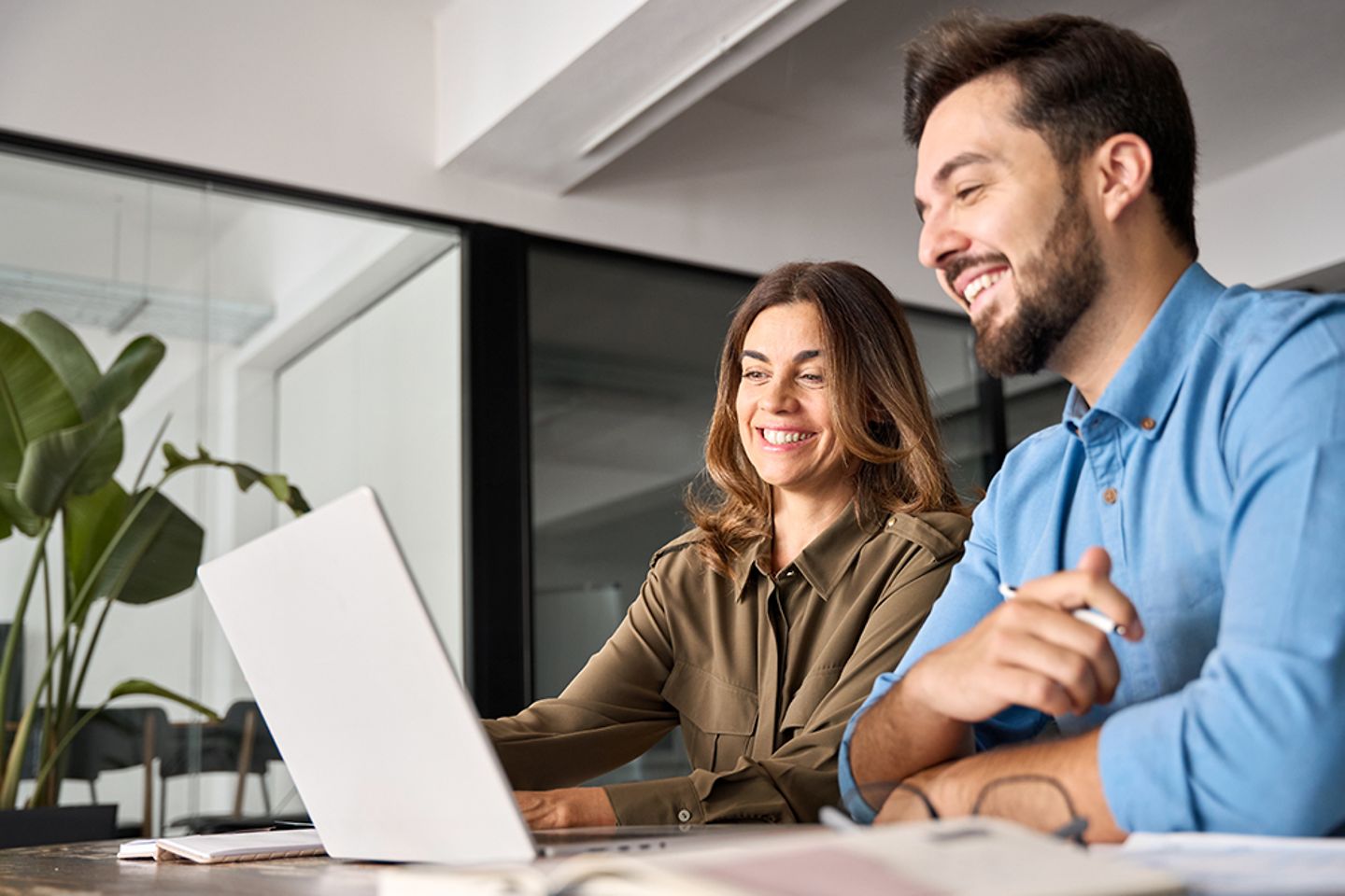 Two smiling professionals talking using laptop computer working in office