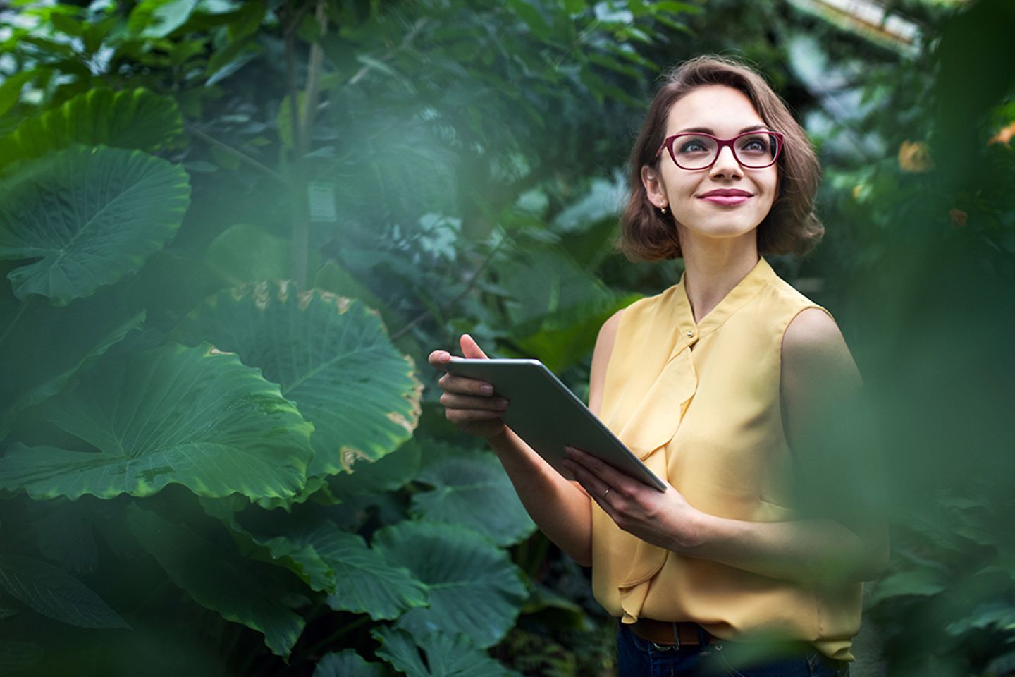 Mulher sorridente com um tablet na mão, cercada por plantas