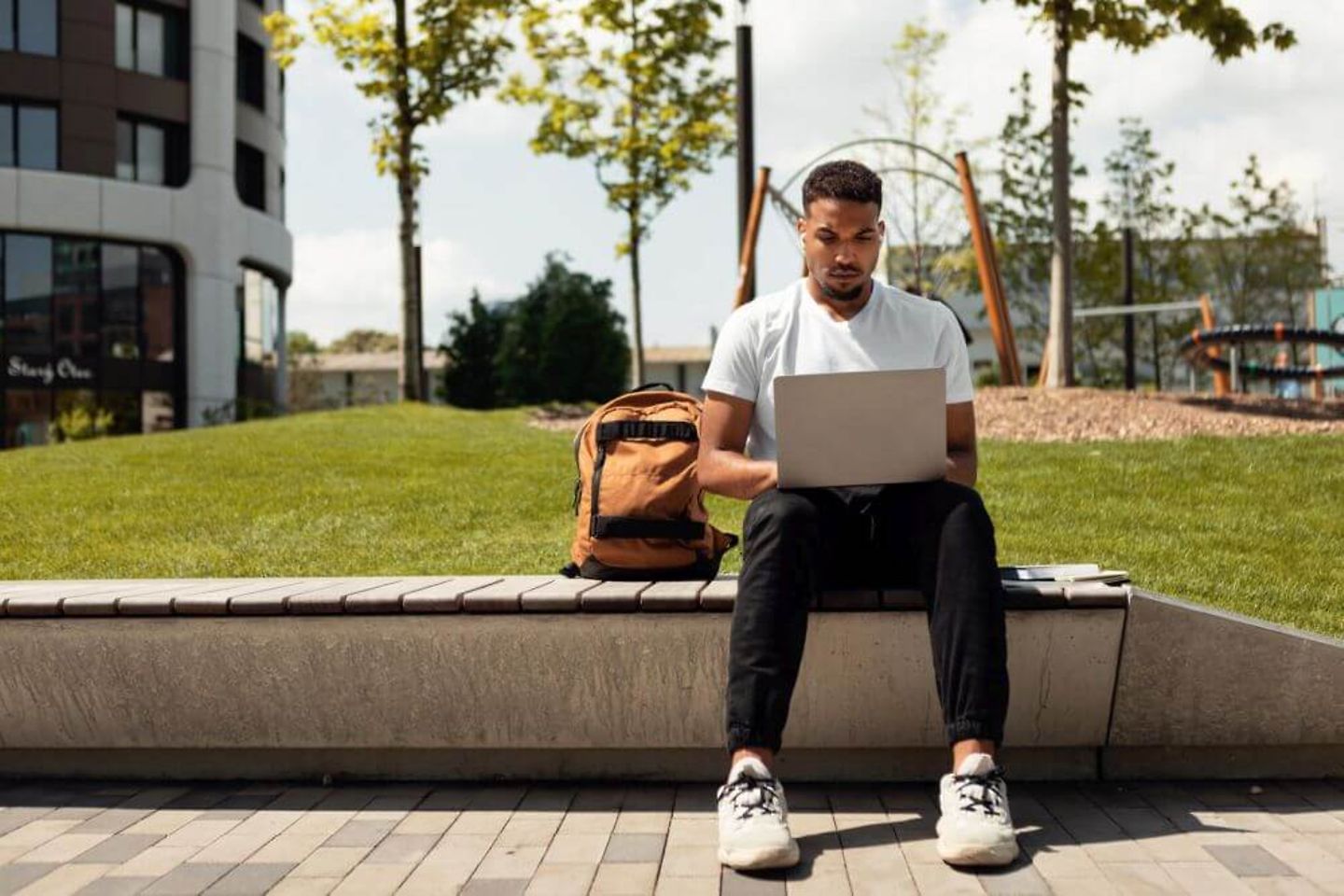 Junger Mann mit Laptop sitzt im Freien auf einer Bank