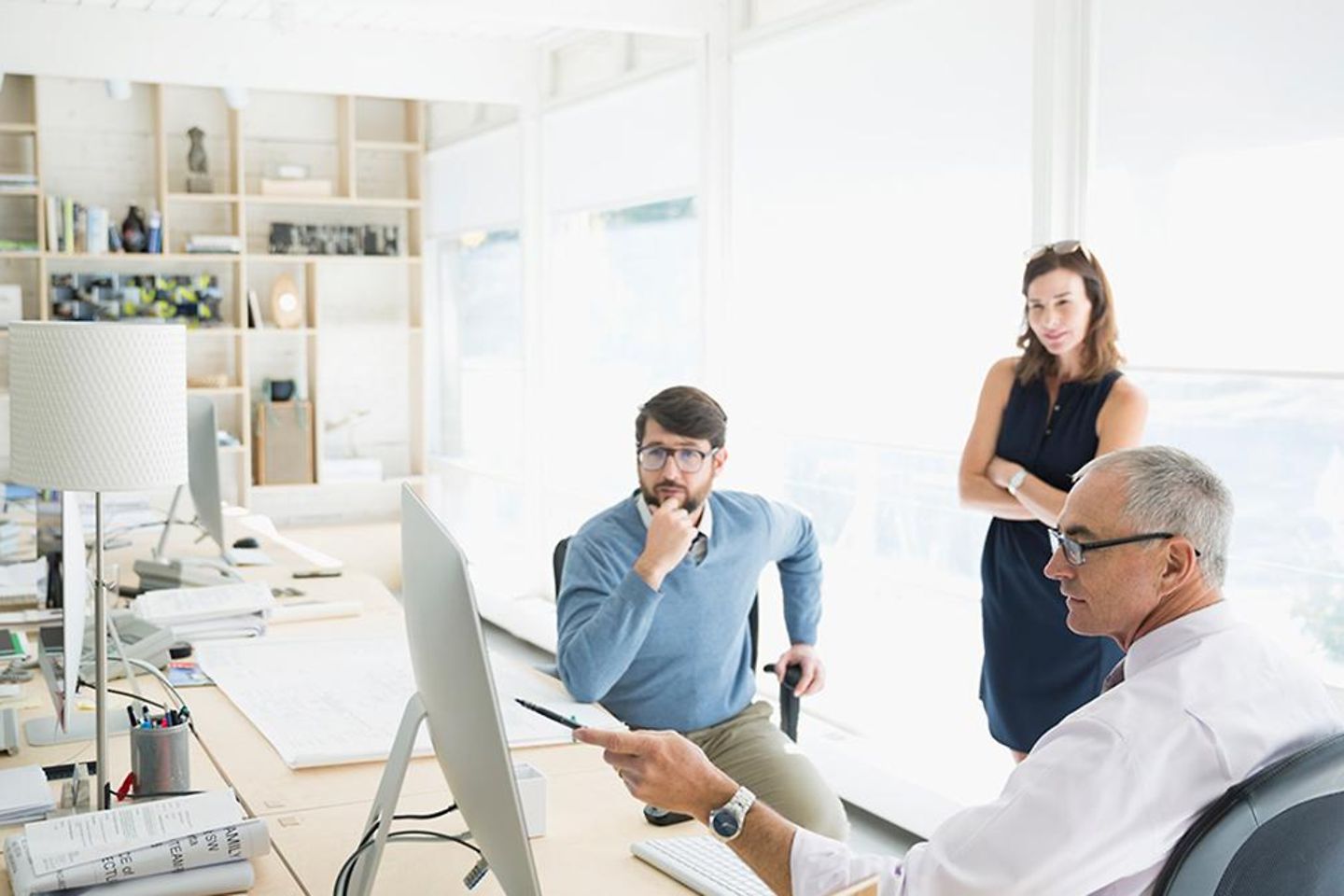 Ein älterer Mann zeigt Mitarbeitern sein Arbeit am Computer