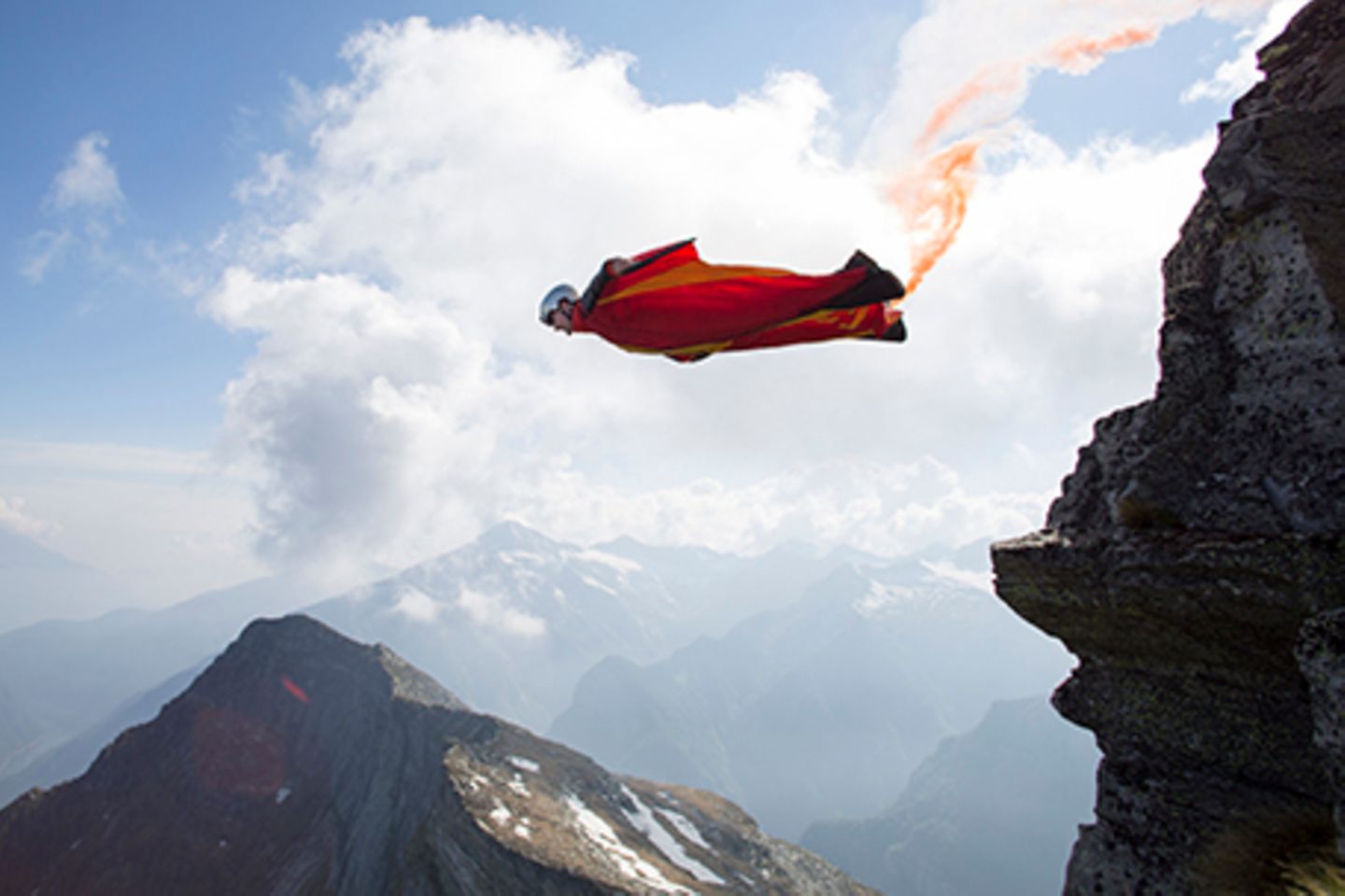 Wingsuit Jumper springt mit rotem Leuchtfeuer von Felsen.