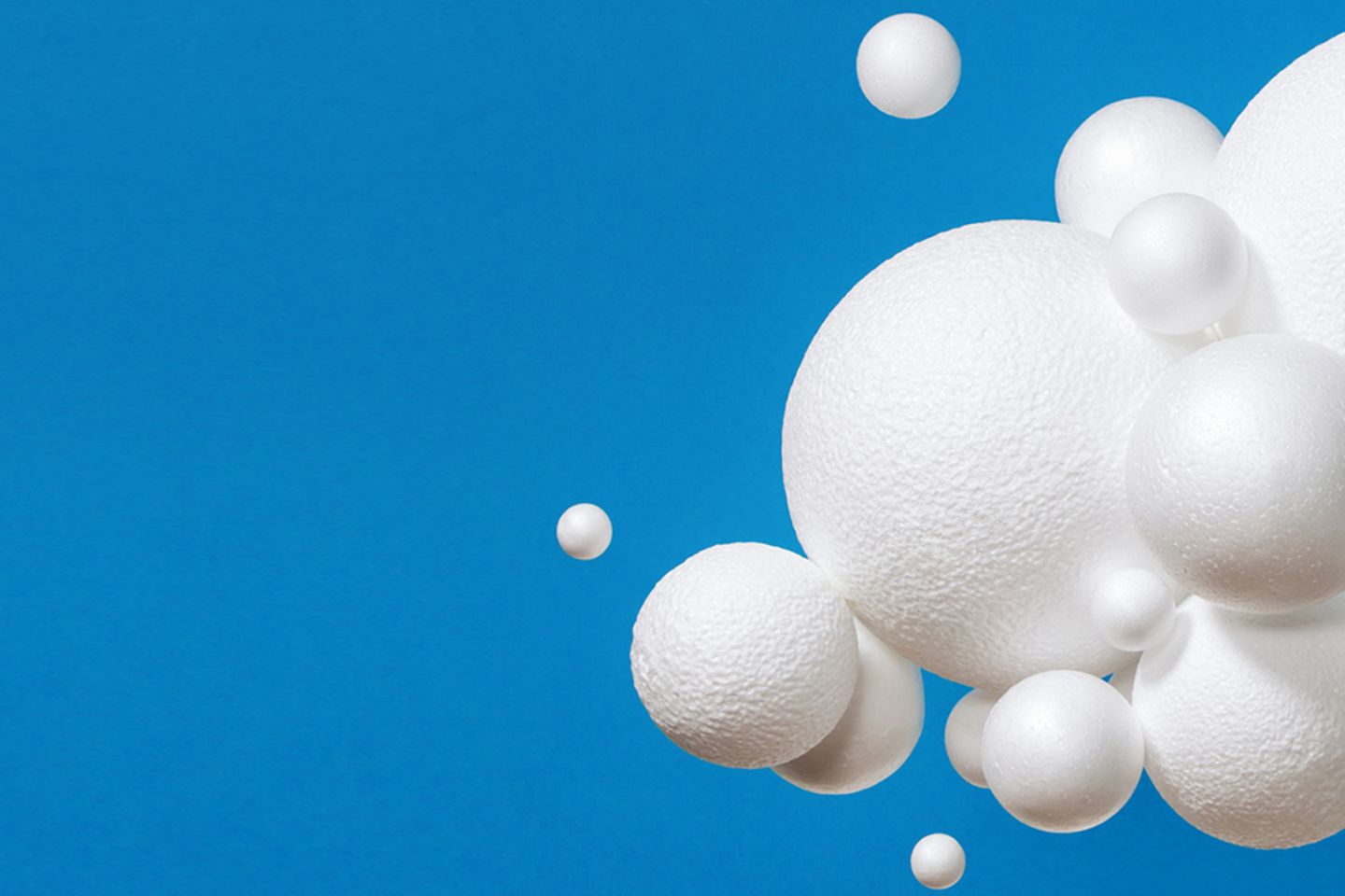 Picture of an artificial cloud in front of a blue background, composed of white spheres of different sizes.
