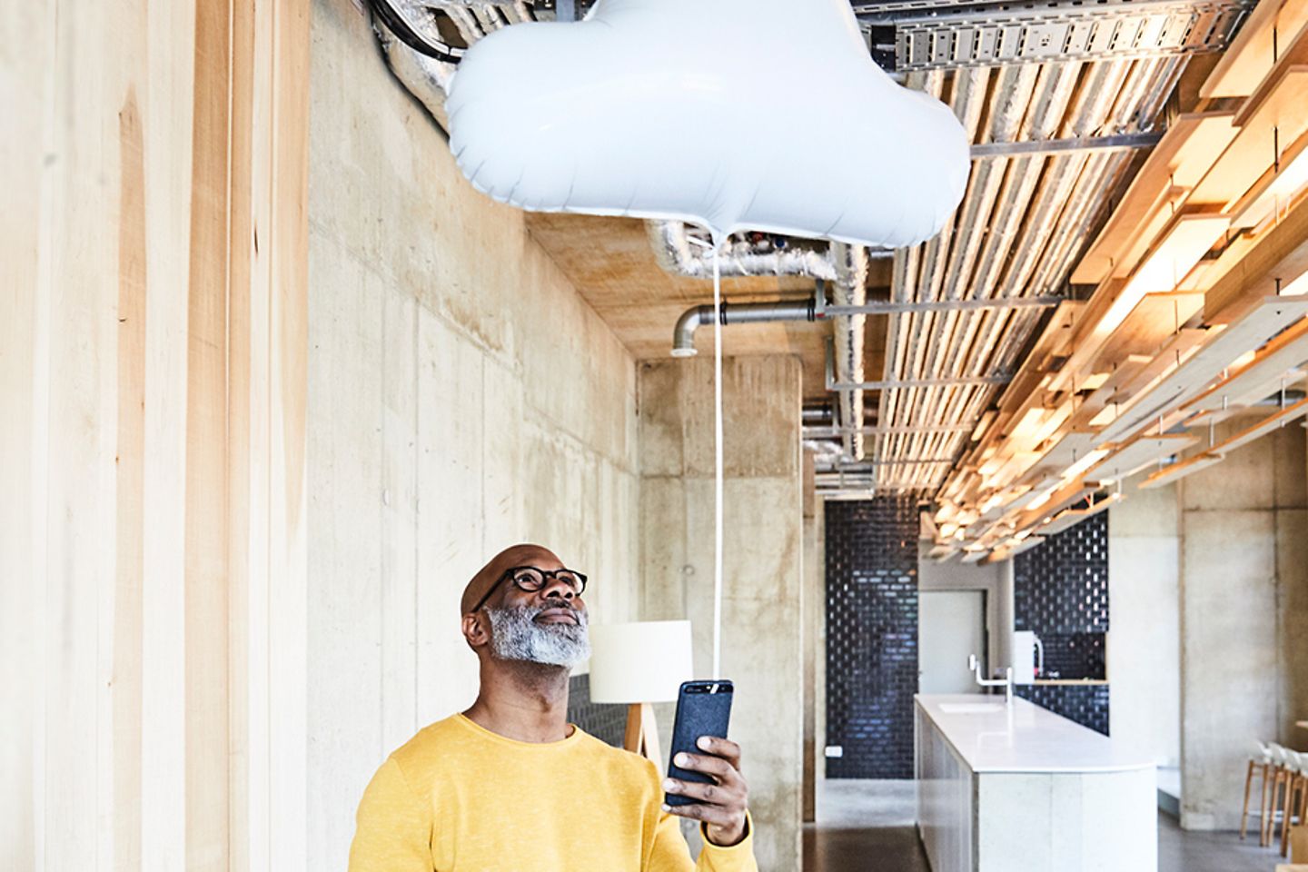 Image of a man in a modern building holding a smartphone with a gas balloon in the shape of a cloud attached to it.