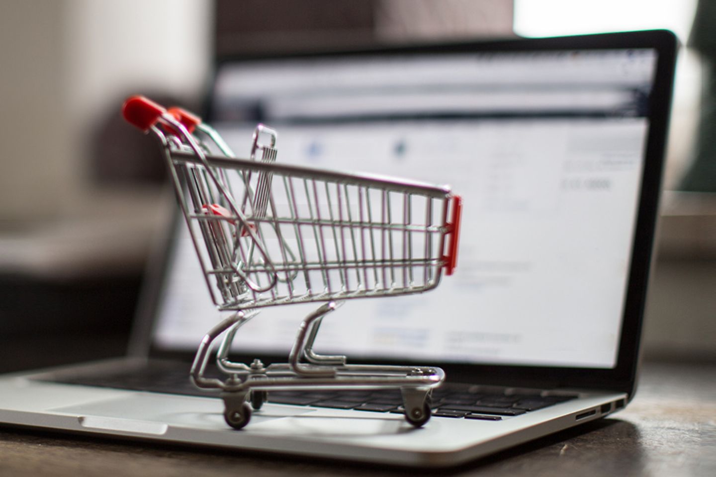 Shopping cart miniature stands on laptop keyboard.