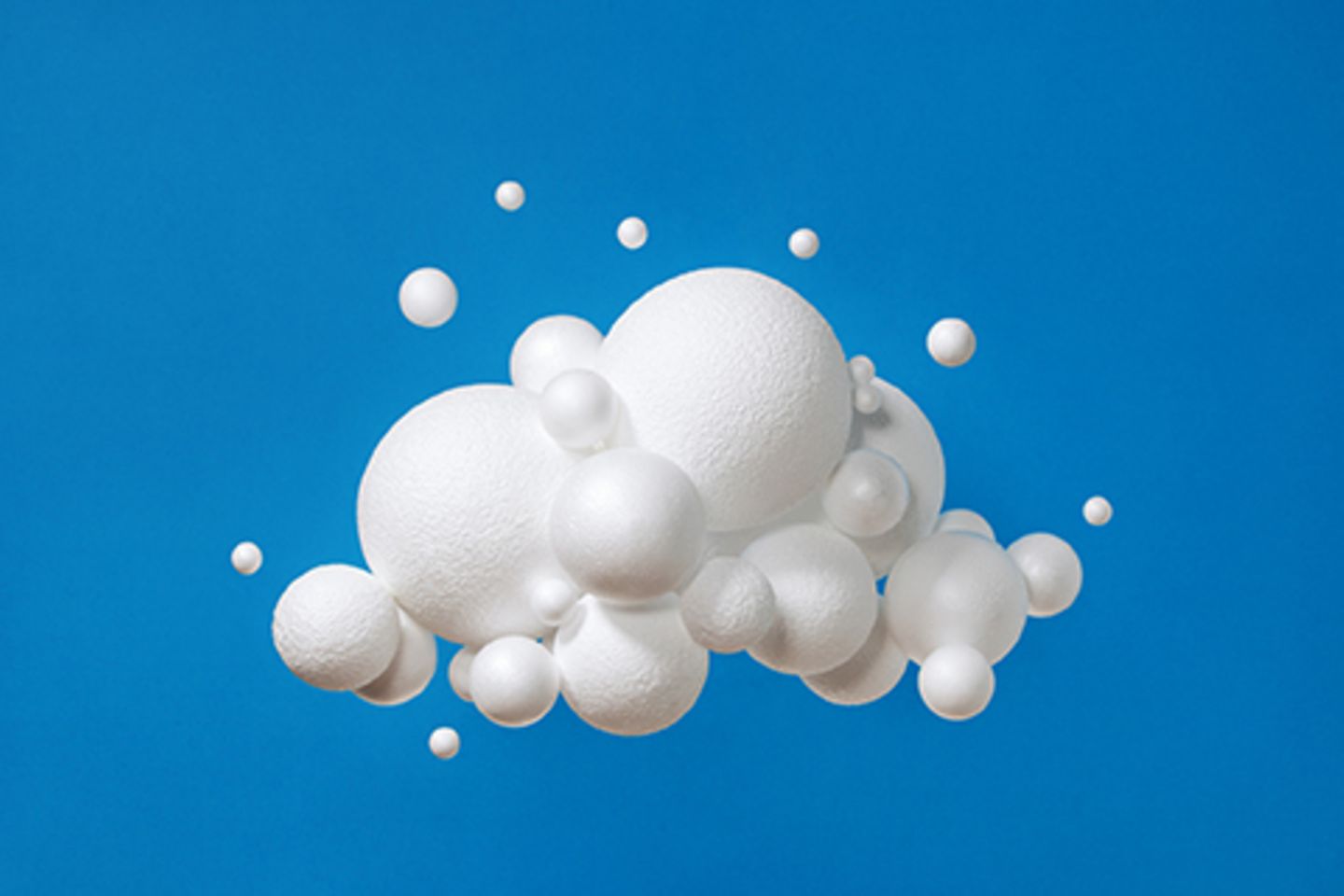 Picture of an artificial cloud in front of a blue background, composed of white spheres of different sizes.