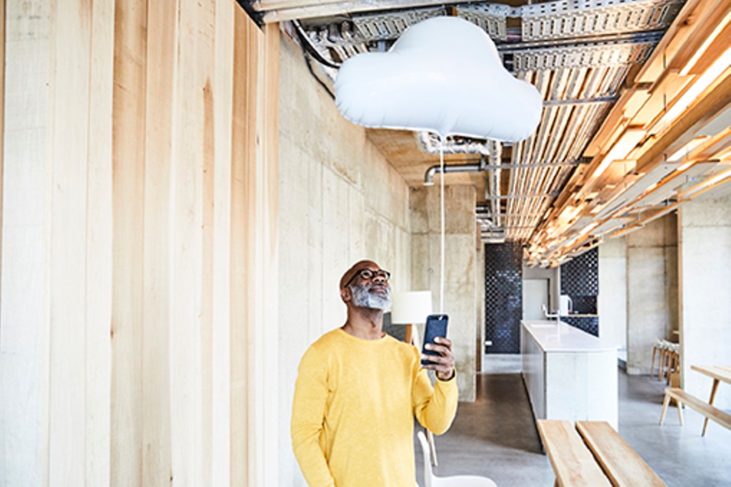Image of a man in a modern building holding a smartphone with a gas balloon in the shape of a cloud attached to it.