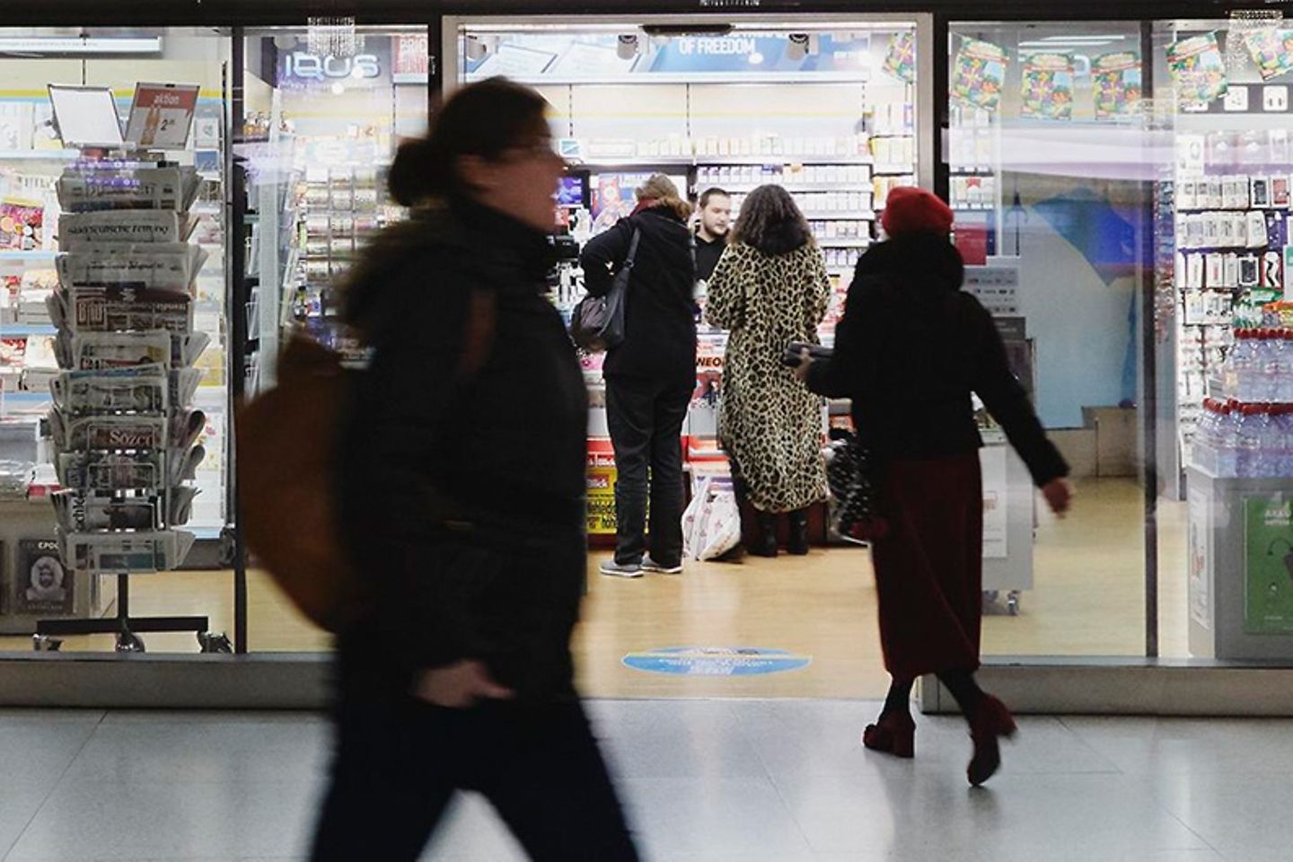 A woman dressed in black passes a kiosk, in which several customers are present.