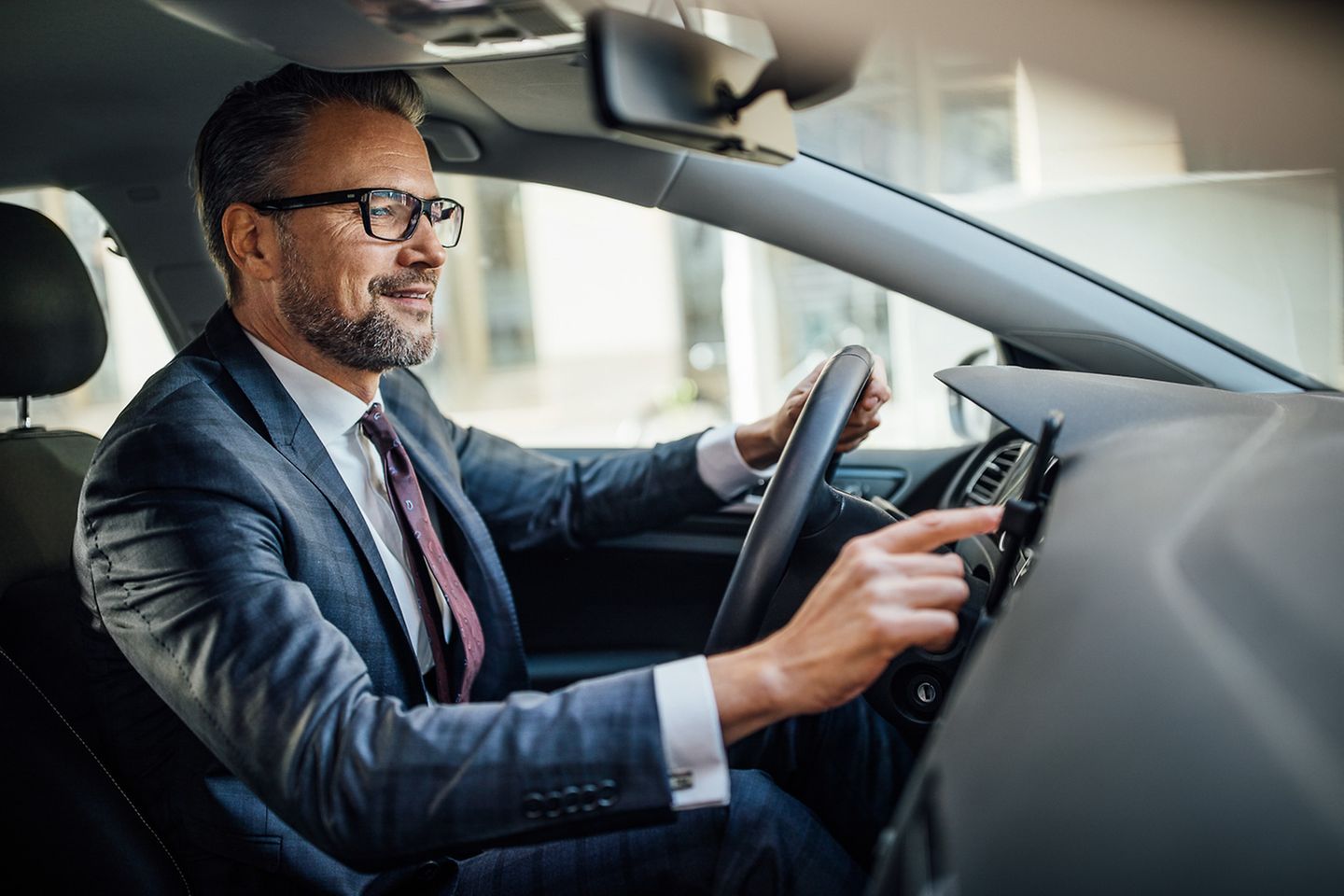  Un homme est assis au volant d’une voiture et utilise son smartphone, fixé au tableau de bord, avec sa main droite.