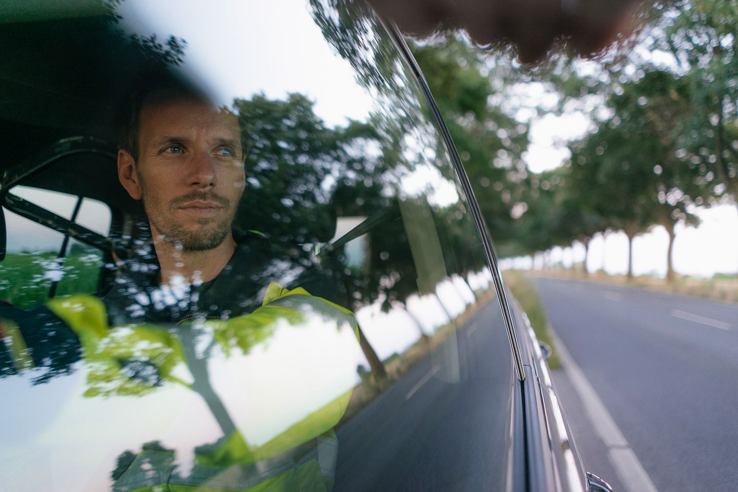 Prise de vue en extérieur d’un homme en voiture, regardant rêveusement par la fenêtre latérale durant le trajet 
