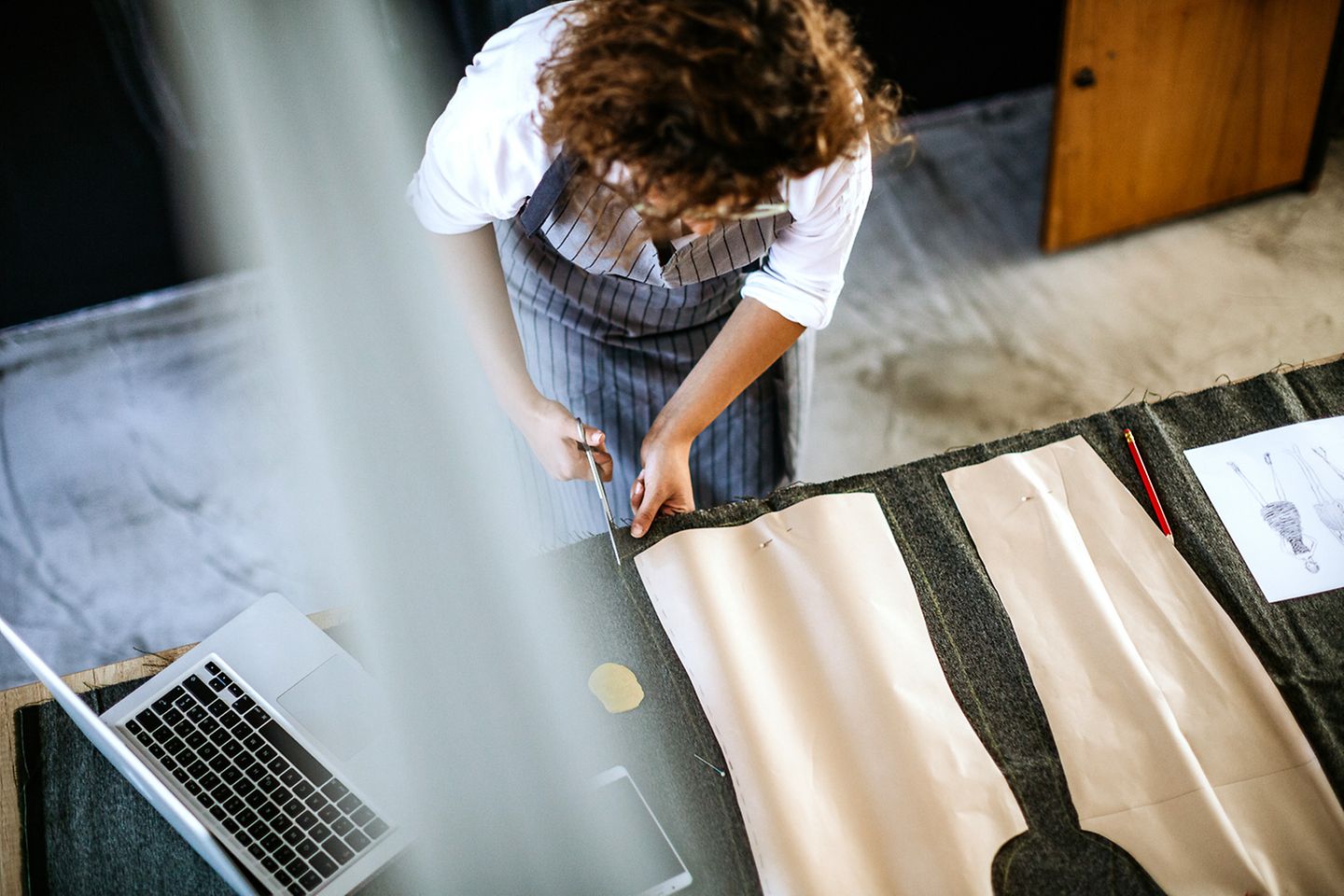 Une couturière vue d’en haut découpe du tissu sur une table.