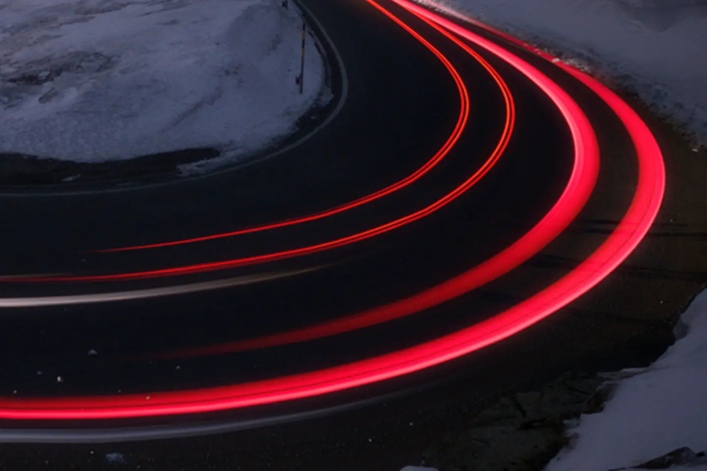 Courbe de 180 degrés la nuit et dans la neige avec des faisceaux lumineux déformés par les feux arrière des voitures