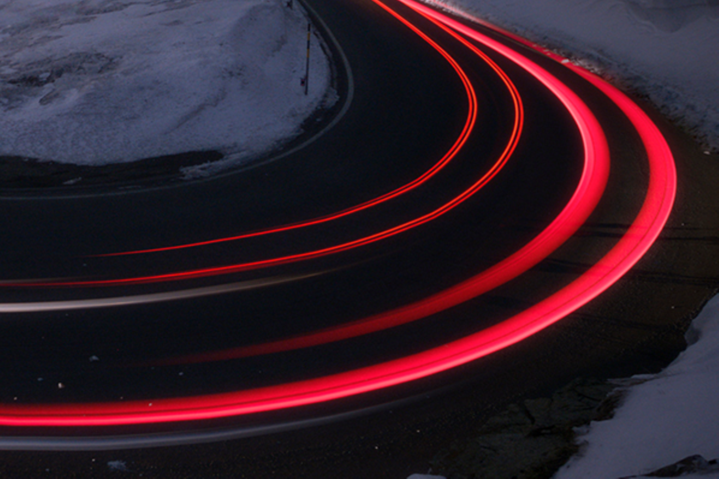 Courbe de 180 degrés la nuit et dans la neige avec des faisceaux lumineux déformés par les feux arrière des voitures