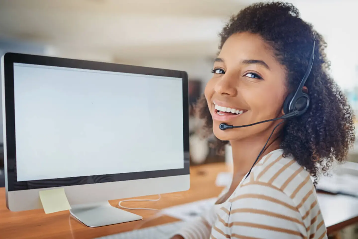 Woman sitting in front of a monitor wearing a headset and smiling